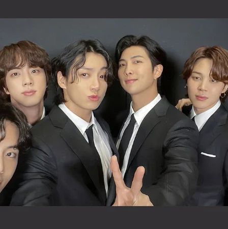 7 integrantes da banda BTS posando juntos para foto vestidos com terno.
