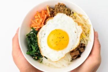 Prato montado de bibimbap com arroz, vegetais e ovo.