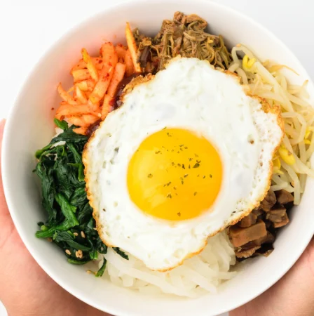 Prato montado de bibimbap com arroz, vegetais e ovo.